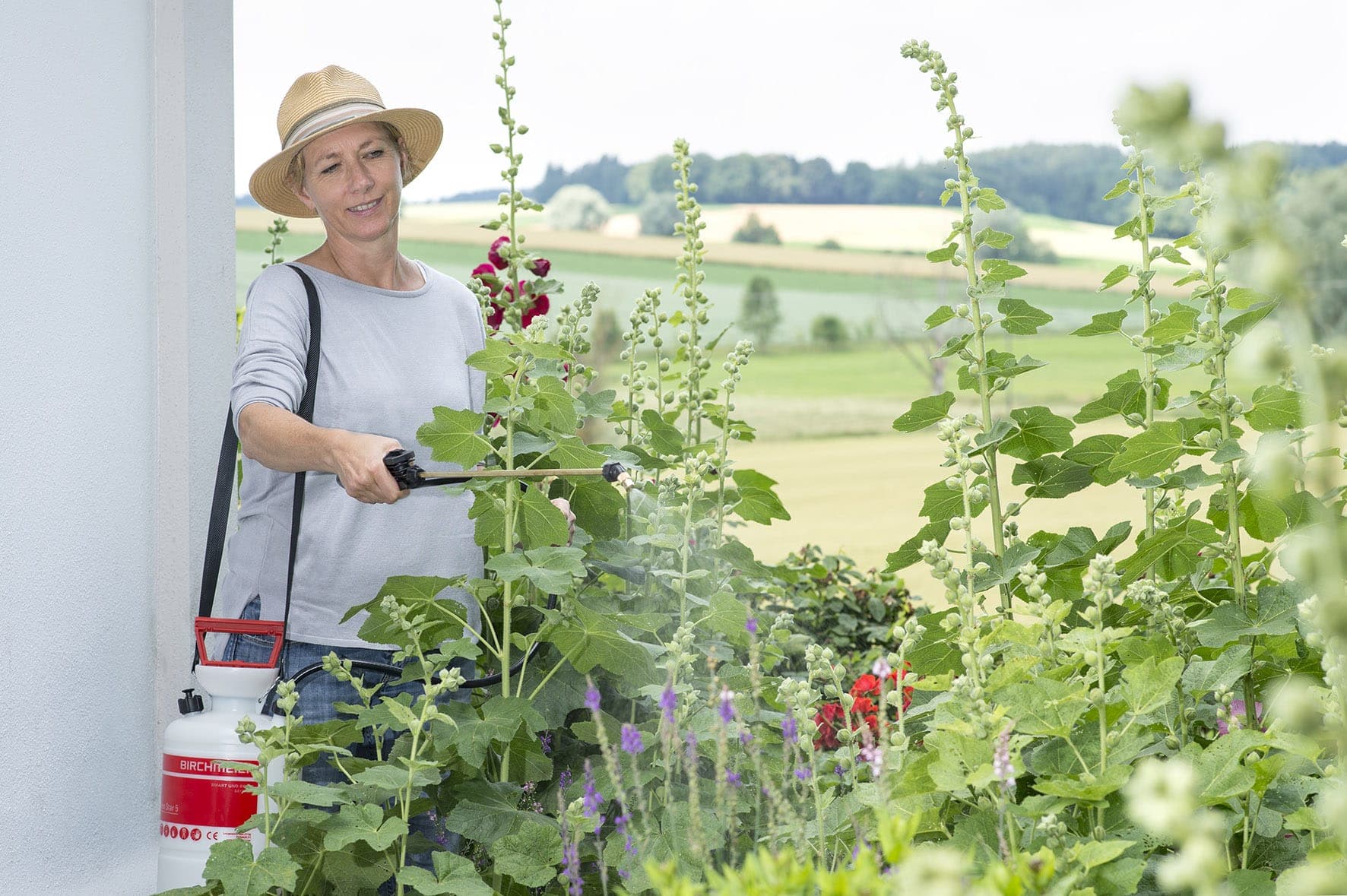 Vrouw met een drukspuit tussen bloeiende planten