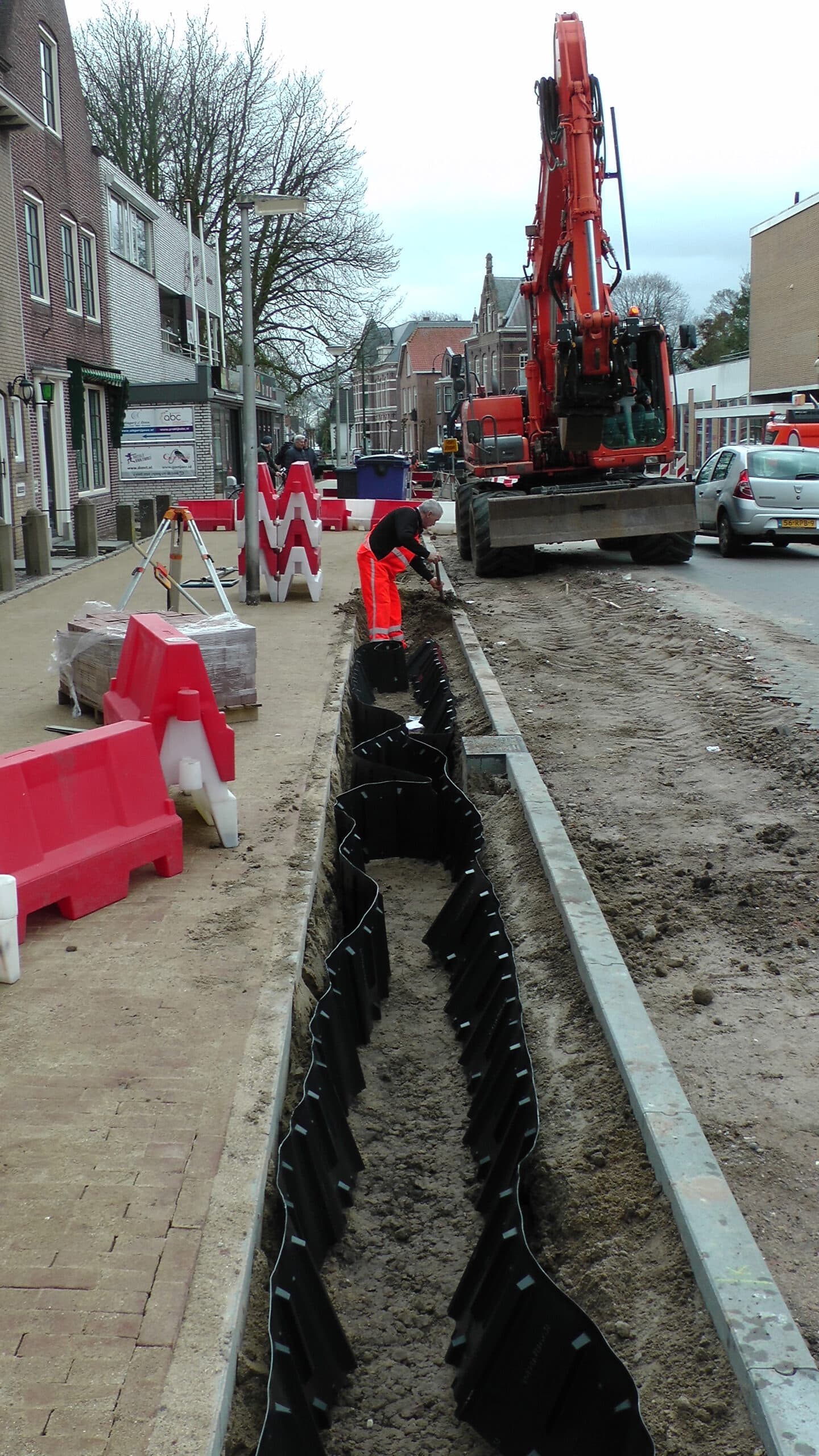 Straatwerf met graafmachine en werfafzetting tijdens de plaatsing van wortelgeleiding